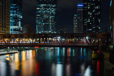 Illuminated bridge over river against skyscrapers