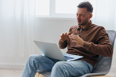 Young woman using laptop while sitting on sofa at home