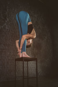 A charming girl in a sports uniform does yoga in an old room with a fireplace and candles