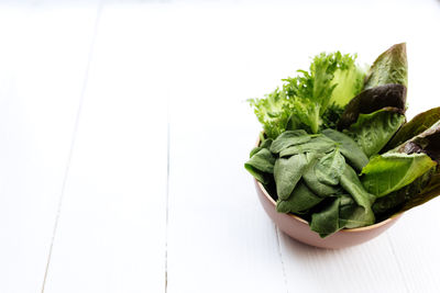 Bowl of fresh green salad leaves of spinach, lettuce, romaine and basil on white wooden background