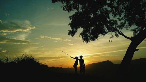 Silhouette people taking selfie by tree against sky during sunset