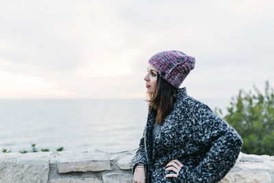 Side view of young woman standing at beach against sky