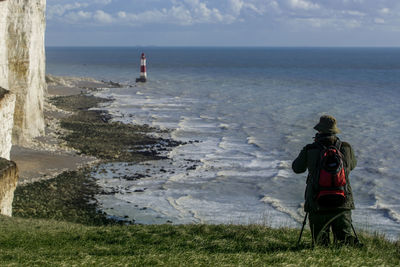 Rear view of man looking at beachy head lighthouse in sea at seven sisters against sky