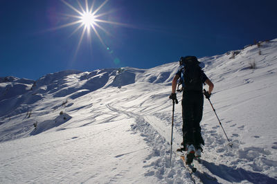 Low angle view of hiker walking on snow covered mountain against bright sky