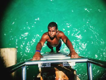 Portrait of shirtless man climbing on ladder in sea