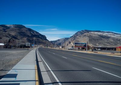 Empty road leading towards mountains against blue sky