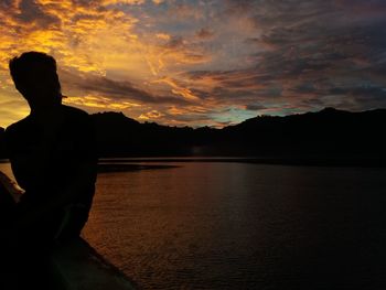 Silhouette man standing by lake against sky during sunset