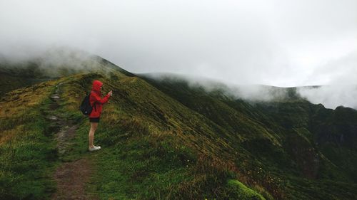 Side view of woman standing on landscape against sky during foggy weather