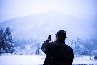 Rear view of man photographing snowfall 