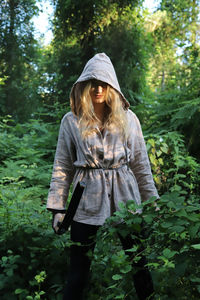 Young woman wearing hooded jacket standing amidst plants in forest