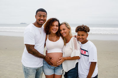 Family posing for maternity photos on beach