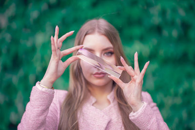 Portrait of beautiful woman holding crystal against plants