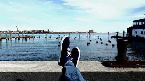 Low section of person wearing shoes at pier against sky