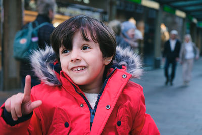 Portrait of cute 4 years old boy with brown hair and red jacket outdoors