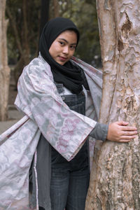 Young woman looking away while standing on tree trunk