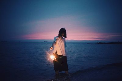 Rear view of man standing against sea at sunset