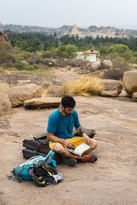 Young man reading book while sitting on land, karnataka, hampi, india