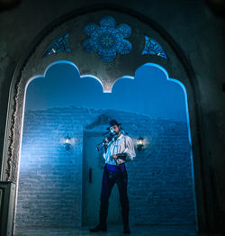 Portrait of man in costume standing against door of abandoned building at night