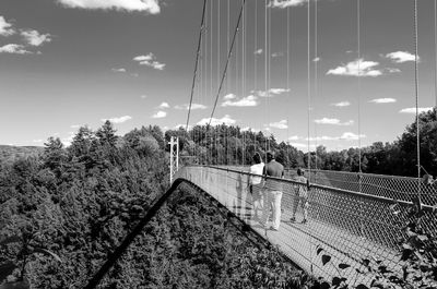 People walking at bridge against sky on sunny day