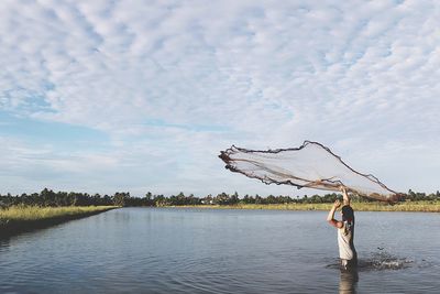 Fisherman throwing net in lake against sky