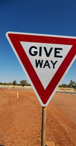 Road sign on field against clear blue sky