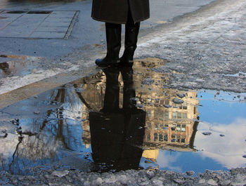 Low section of person reflecting in puddle on street