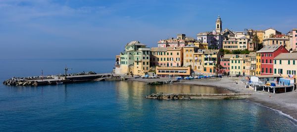 Buildings by sea against blue sky