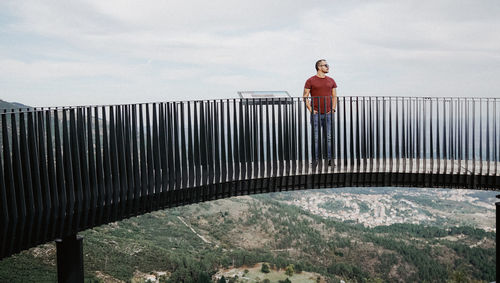 Man standing on railing against sky