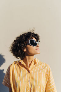 Woman with curly hair wearing alien sunglasses in front of wall