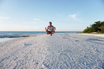 Man meditating on beach against sky