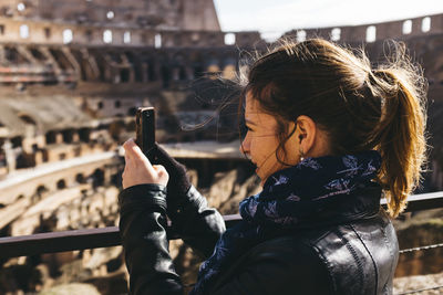 Young woman holding camera while standing on table