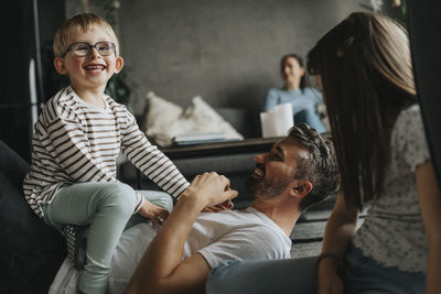 Cheerful children having fun with father lying down on floor at home