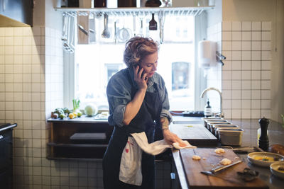 Female chef talking on mobile phone while cleaning kitchen counter in restaurant