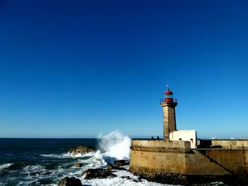 Lighthouse by sea against blue sky