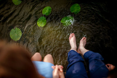 Low section of couple sitting by lake