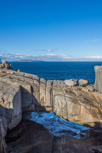 Scenic view of rocks by sea against blue sky