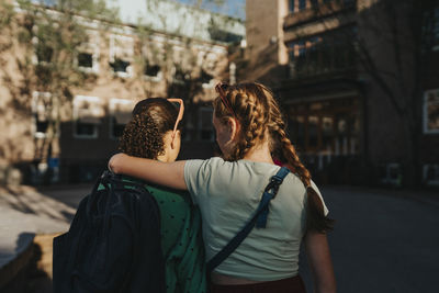 Rear view of girl walking with arm around female friend at school campus