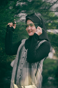 Smiling young woman holding tree branch while standing outdoors