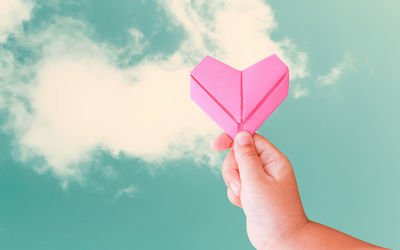 Close-up of hand holding heart shape against sky