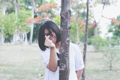 Woman gesturing while standing behind tree trunk at park