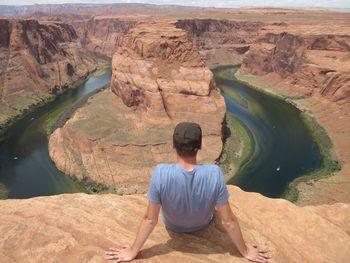 Rear view of man relaxing on cliff in front of horseshoe bend