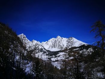 Low angle view of snowcapped mountains against blue sky