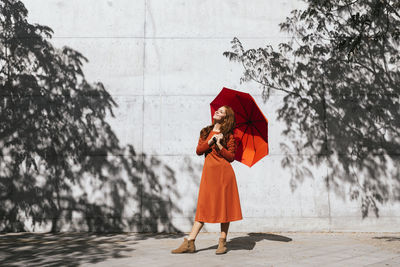 Woman holding umbrella standing by tree during rainy season