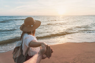 Woman holding hands while standing at beach during sunset