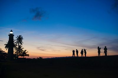 Silhouette people by palm trees against sky during sunset