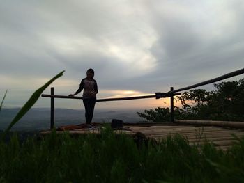 Woman standing by railing against sky during sunset