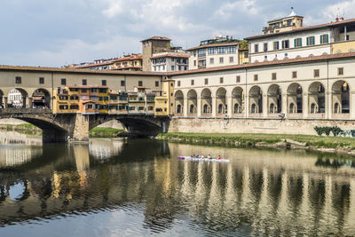 Bridge over river by buildings against sky