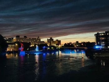 Illuminated buildings by river against sky at night