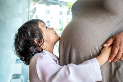 Side view of girl embracing pregnant mother at home