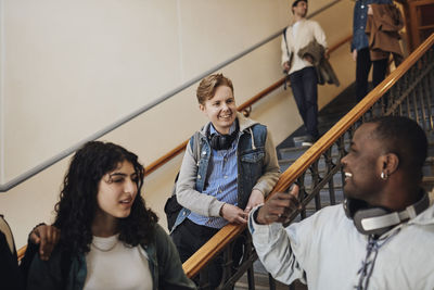 Smiling male student talking with friend while leaning on railing in university